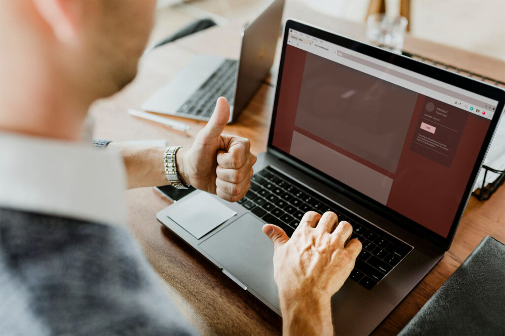 Persona frente a un portátil con el pulgar levantado y una web con errores en pantalla, representando la recuperación exitosa de un proyecto WordPress problemático.