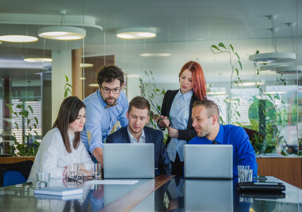 Equipo de cinco personas reunido en una oficina moderna, trabajando juntos frente a portátiles