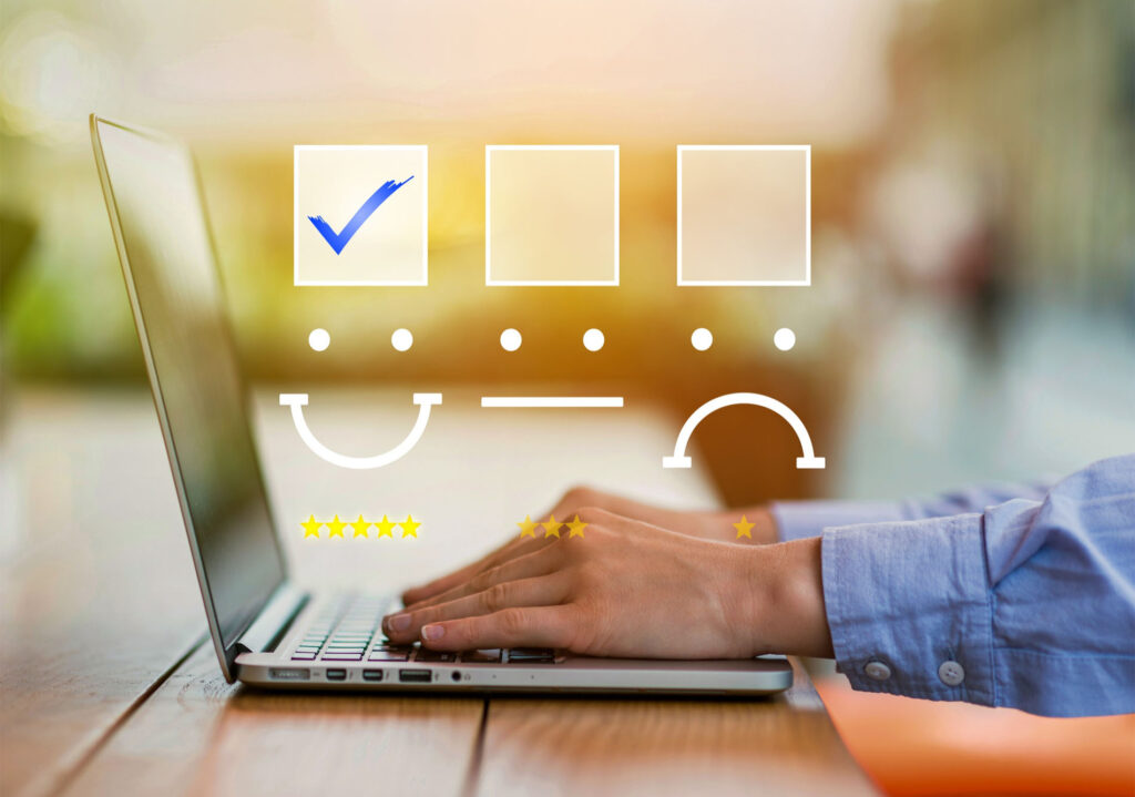 Persona escribiendo en un portátil con iconos superpuestos de encuesta de satisfacción, incluyendo caras feliz, neutra y triste, estrellas de valoración y casillas de verificación
